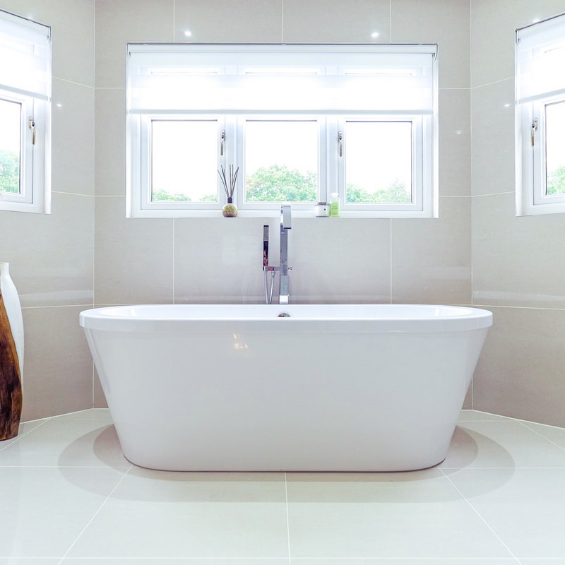 A freestanding white bathtub beneath a triple window in a freshly painted, tiled bathroom.