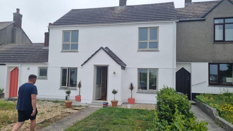 A semi-detached house with freshly painted white render, grey window frames, and potted plants by the front door.