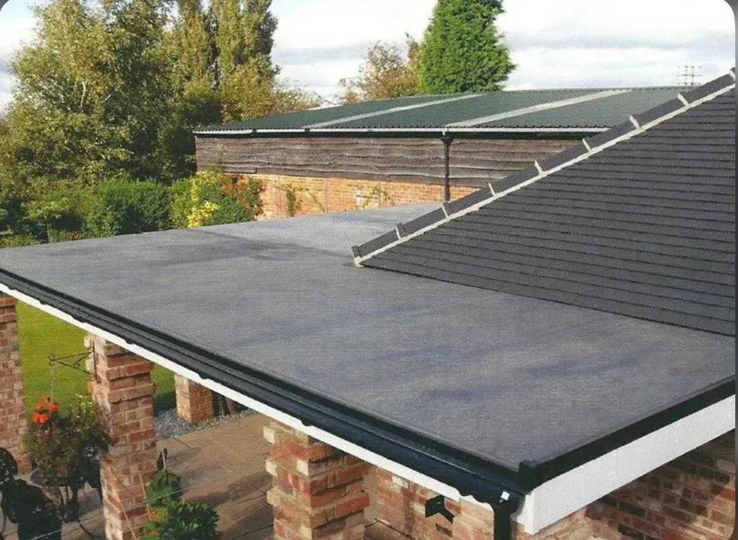 A grey flat roof covering over a brick pillared patio area, adjoining a tiled pitched roof and garden.