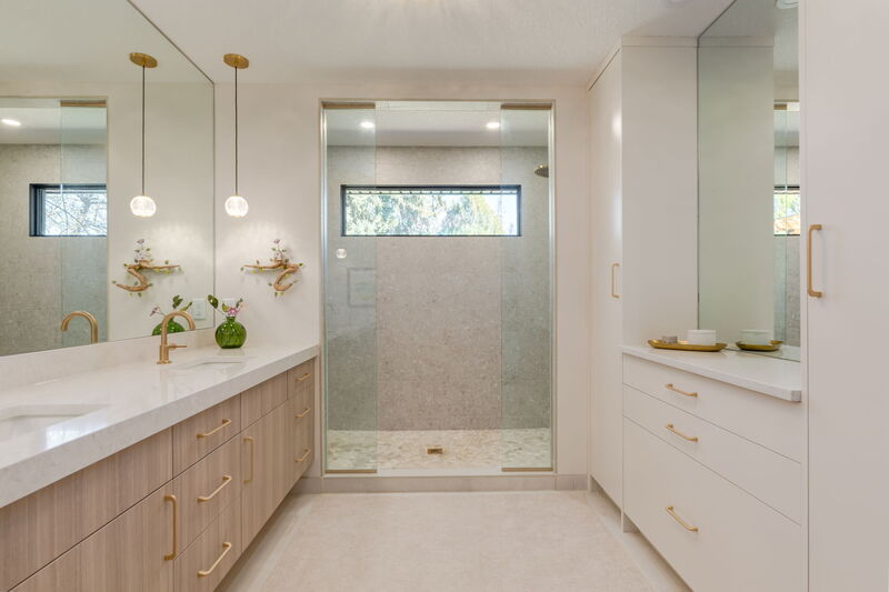 A modern ensuite bathroom with a glass-enclosed shower, twin gold-tap sinks, and a wood-toned vanity unit.