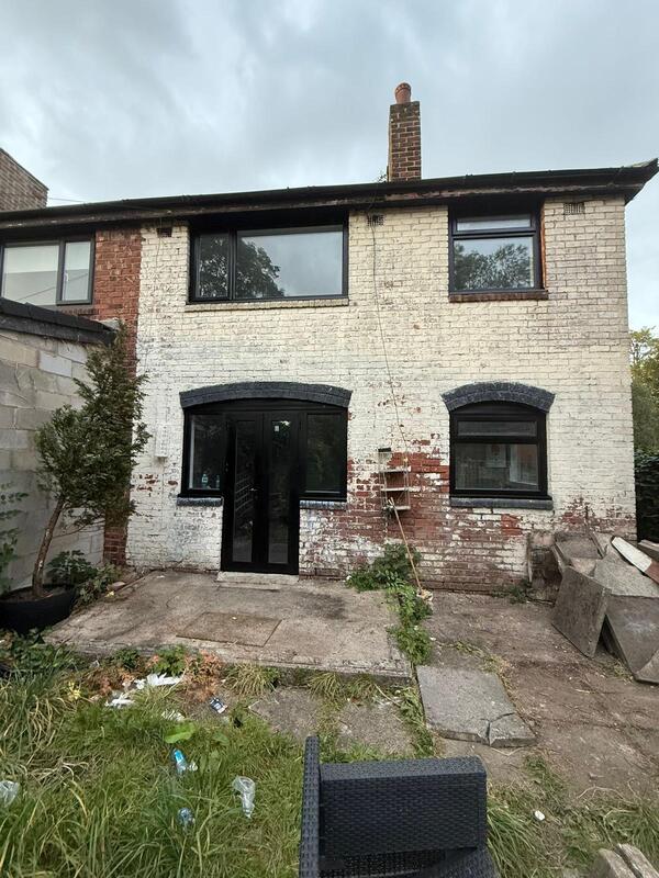 Rear of a house with patched brickwork and black window frames before a rear extension