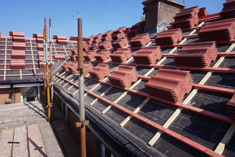 Stacks of red concrete roof tiles laid out on timber battens during a pitched roof installation.